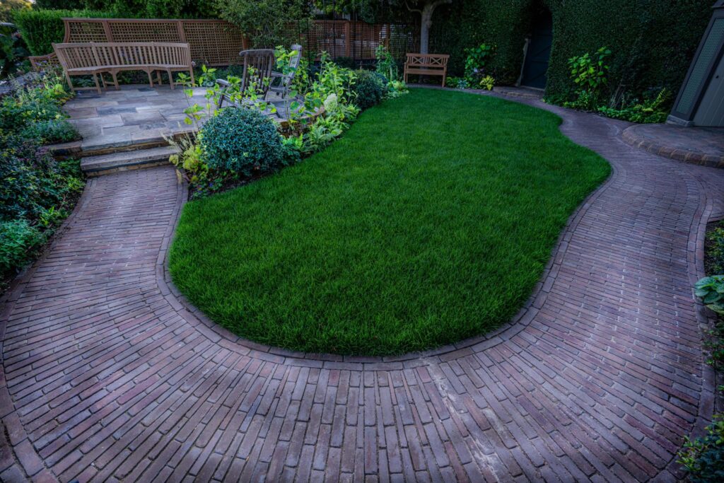 Our Abbey Dark Multi clay pavers form a circular path that lead to a small seating area and surrounds a grassed area. 