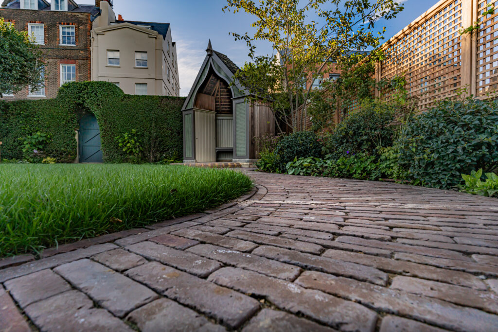 Our Abbey Dark Multi Clay Pavers are used to create a curved pathway. Hedges can be seen in the back ground, as well as fencing and planting. 