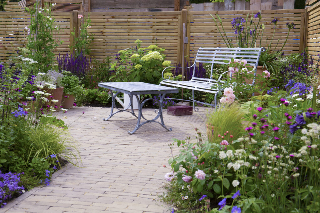 Our Gromo Antica Clay Pavers create a small courtyard that is surrounded by colourful planting and has a metal table and bench seating area. 